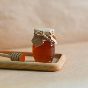 A homemade jar of honey with a rustic wrapping on a wooden tray, showcasing natural sweetness.