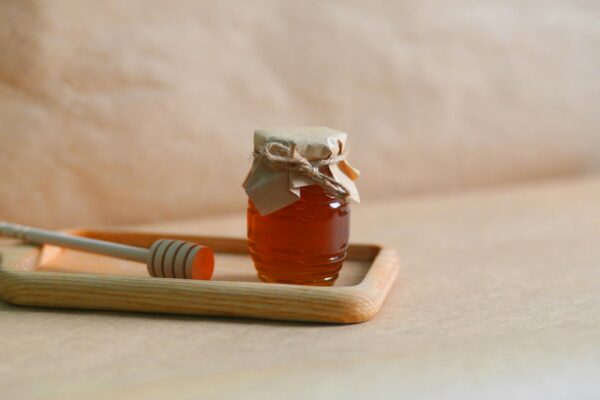 A homemade jar of honey with a rustic wrapping on a wooden tray, showcasing natural sweetness.