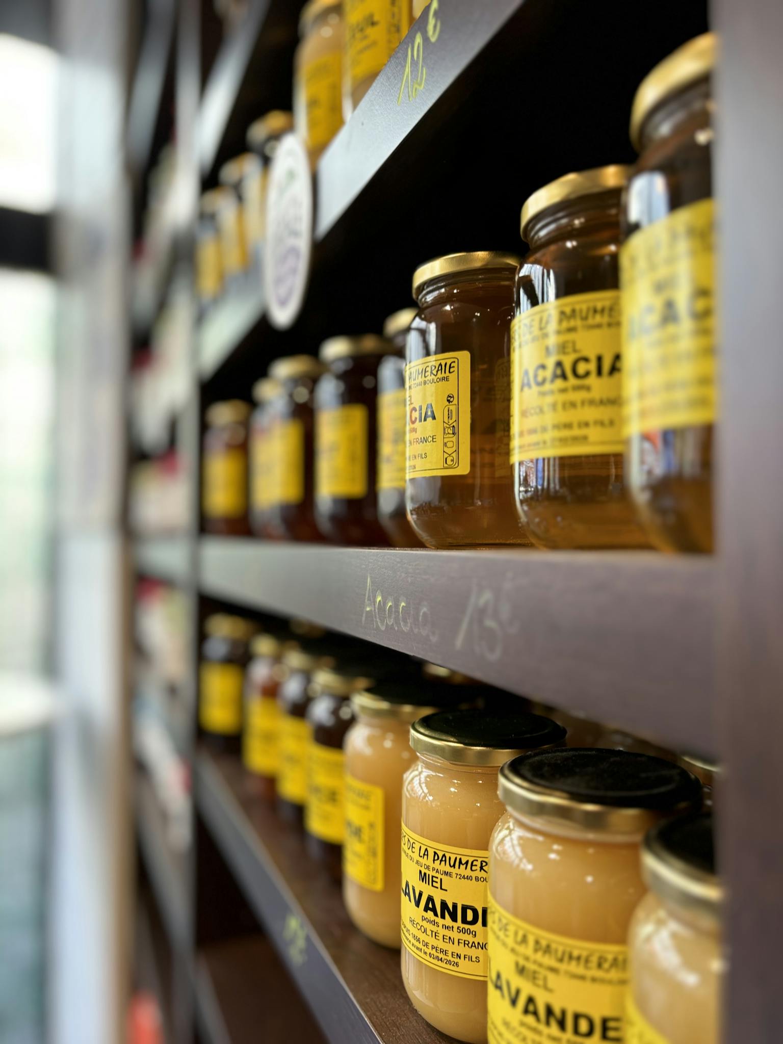 Rows of honey jars with yellow labels neatly stacked on wooden shelves in a Paris shop.