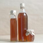 Still life composition of glass bottles and a jar filled with honey, emphasizing rustic charm.